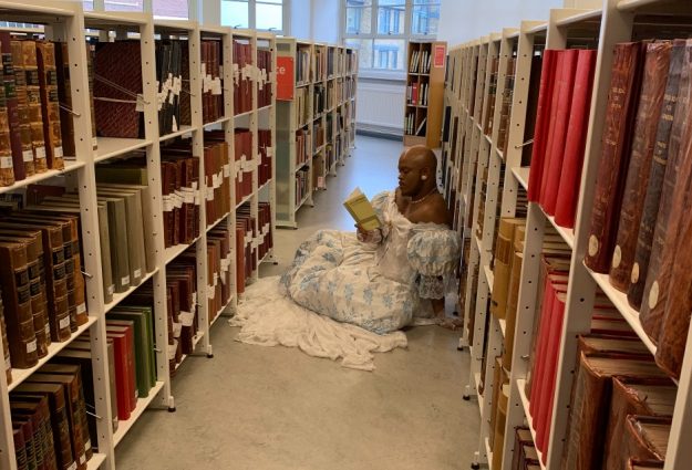 An image of the artist Lasana Shabazz reading books in a library