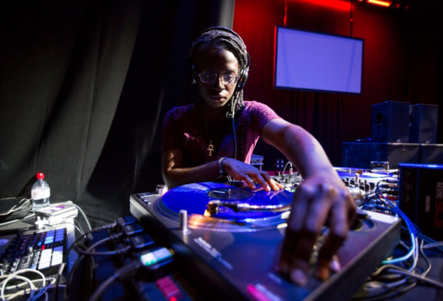 A photo of DJ Niknak in action on the turntable; a young black woman concentraing with a serious expression on spinning records